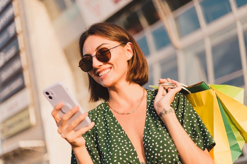 woman-sunset-with-colorful-shopping-bags-parking-lot-by-shopping-mall-happy-with-mobile-phone